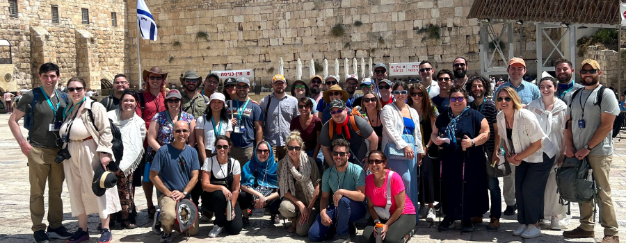 A group of people posing in front of the Western Wall in Jerusalem. Togethering Israel is relevant.