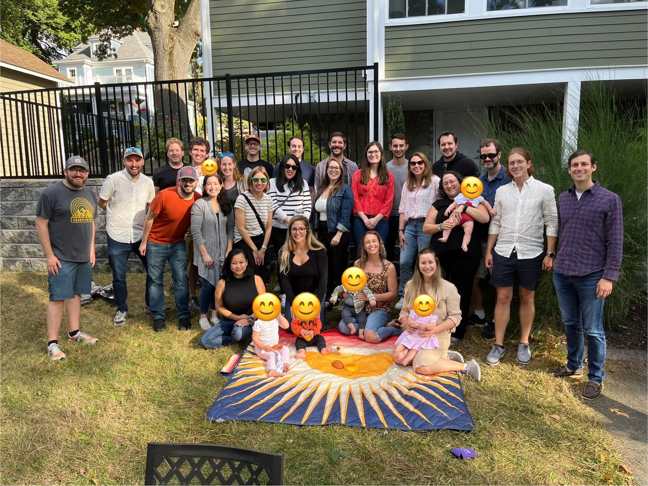 A group of people pose outdoors on a lawn, some with emoji-covered faces.