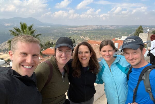 Five people smiling outdoors with a scenic mountain and forest view in the background. 18doors.