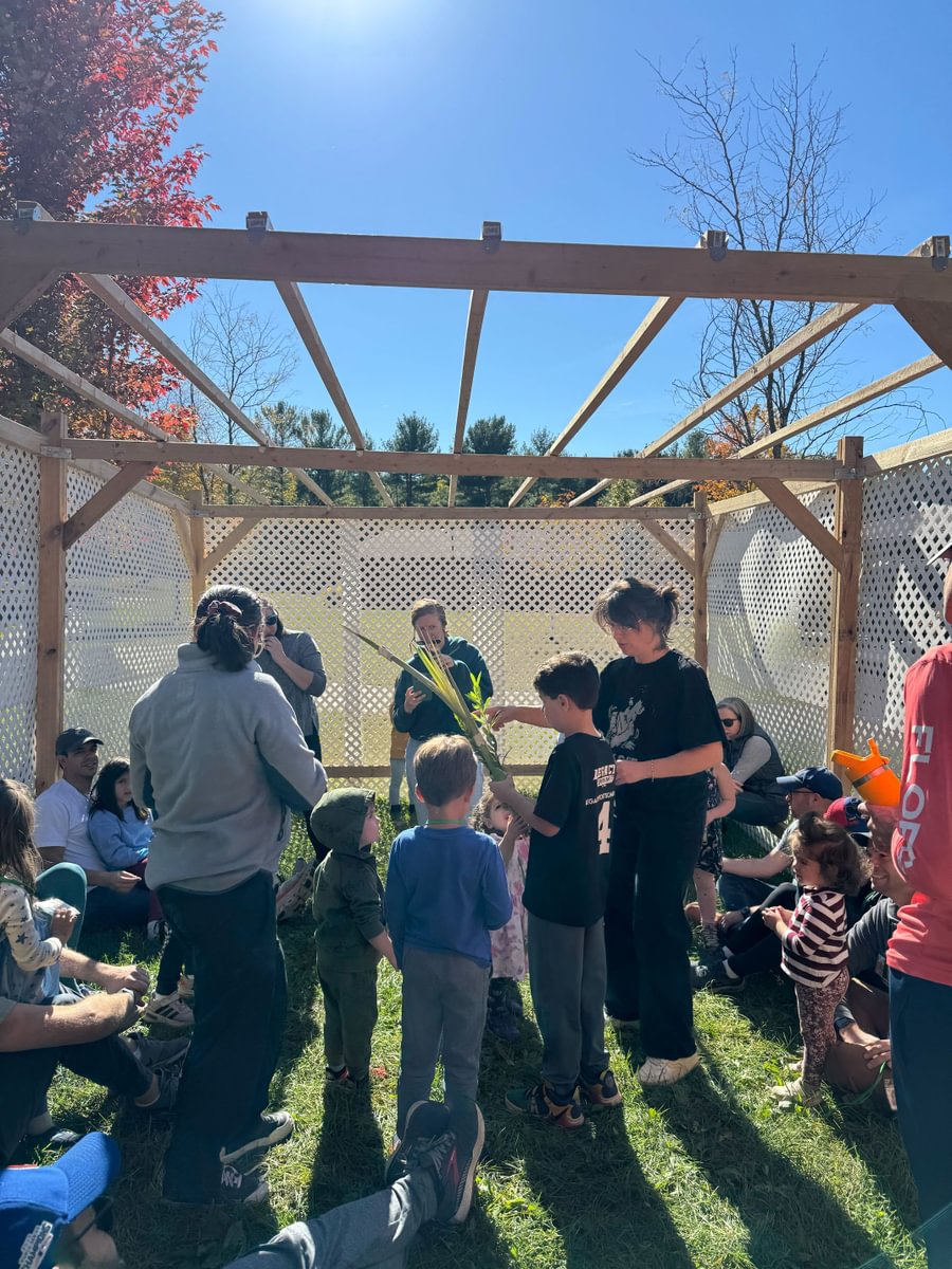 People gathered in a sukkah under sunny skies, participating in Sukkot activities.