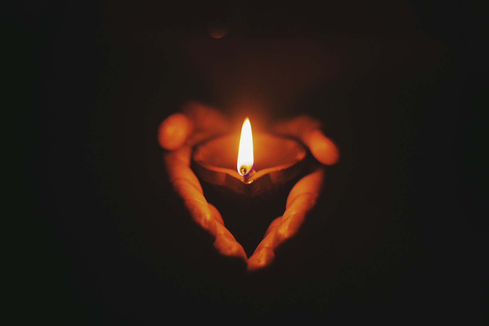 A candle held in cupped hands, creating a heart shape in the darkness.