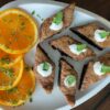 Sliced oranges with herbs and triangular cakes topped with cream and mint on a white plate.