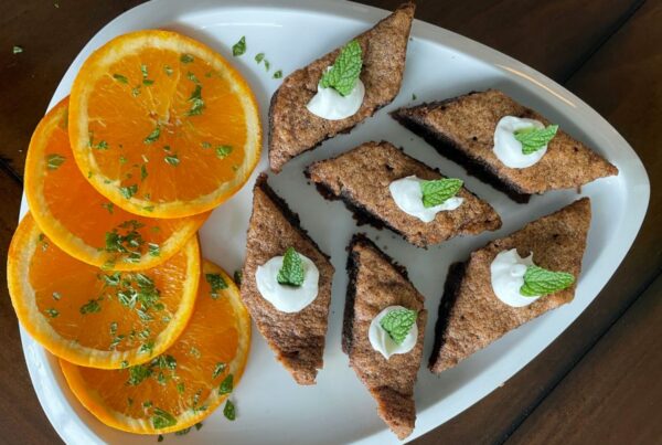 Sliced oranges with herbs and triangular cakes topped with cream and mint on a white plate.